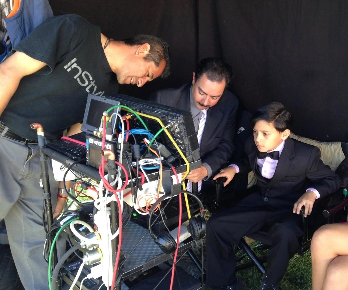 Ethan in a suit sitting with the director at the camera monitors